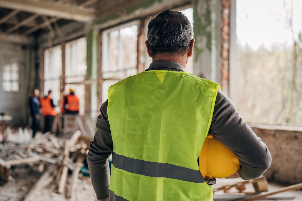 Foreman in high-visibility vest supervises workers fitting windows in a  construction site